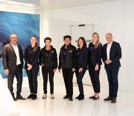 Sieben Teammitglieder in Business- und Arbeitskleidung posieren in modernem, weißem Innenraum. | © Foto Christine