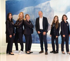 Sechs Teammitglieder in Businesskleidung posieren vor einer blauen Wand mit Eisberg-Motiv. | © Foto Christine