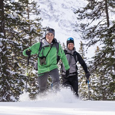 Zwei Männer stapfen mit Schneeschuhen durch tiefen Schnee im Wald. | © Ferienregion Nationalpark Hohe Tauern - Branislav Rohal